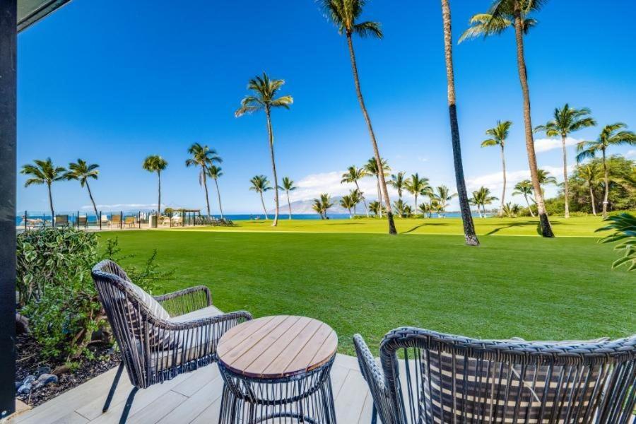 a patio with chairs and a table and a lawn with palm trees at KIHEI SURFSIDE #110 condo in Wailea