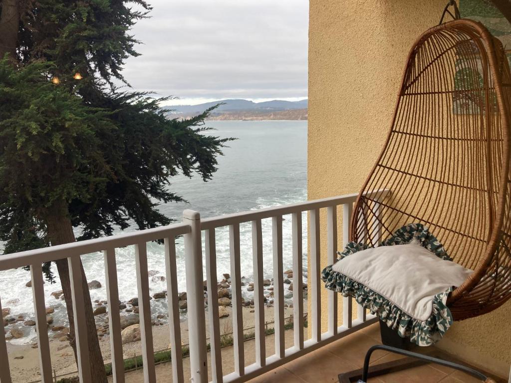 une chaise en rotin assise sur un balcon donnant sur l'océan dans l'établissement ALOJAMIENTO FRENTE AL MAR, CONDOMINIO BAHIA PELICANOS, à Puchuncaví