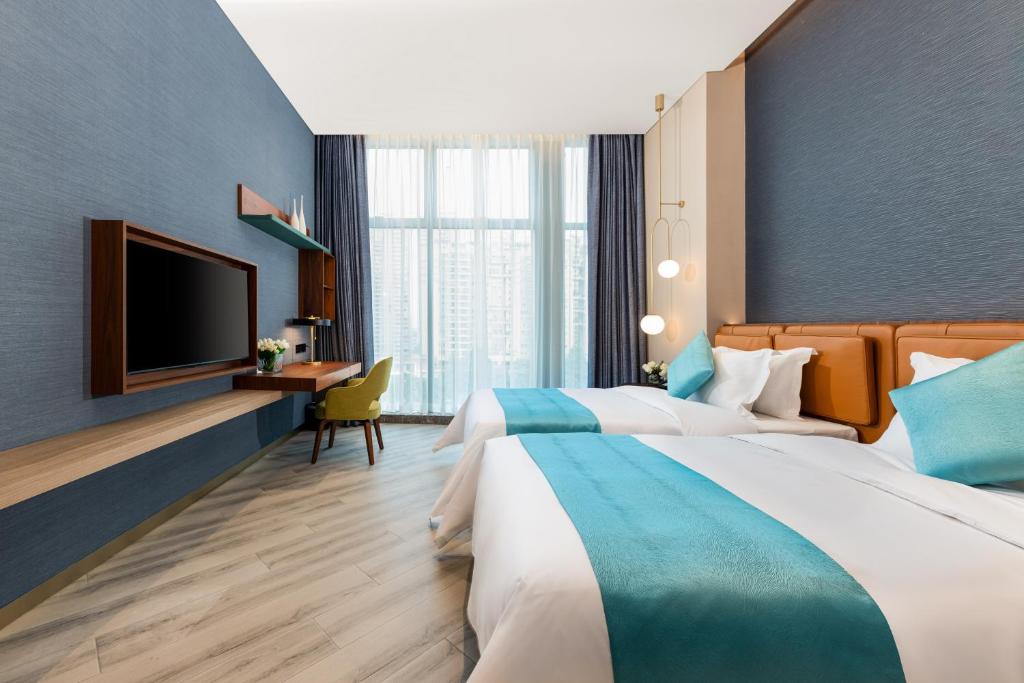 two beds in a hotel room with a flat screen tv at Sha Zhi Ye Serviced Apartment Hotel - Houjie Wanda Plaza Liaoxia Subway Station in Dongguan