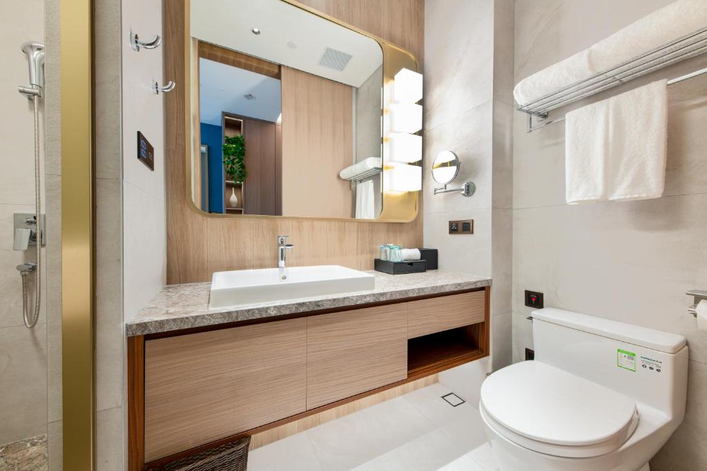 a bathroom with a toilet and a sink and a mirror at Sha Zhi Ye Serviced Apartment Hotel - Houjie Wanda Plaza Liaoxia Subway Station in Dongguan