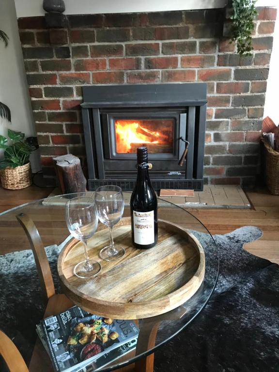 uma garrafa de vinho e dois copos numa mesa em frente a uma lareira em High Country Retreat em Jamieson