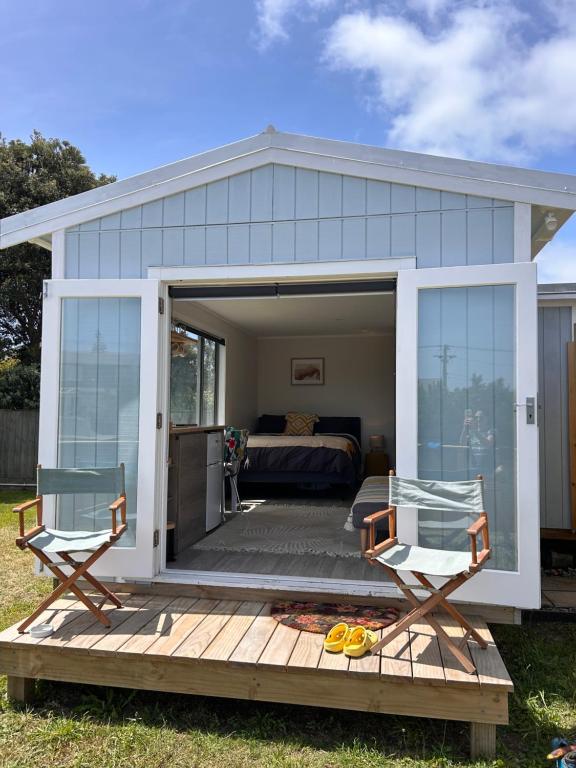 Otaki BeachにあるKowhai Landing Beach Cabinのベッド1台、デッキ(椅子2脚付)