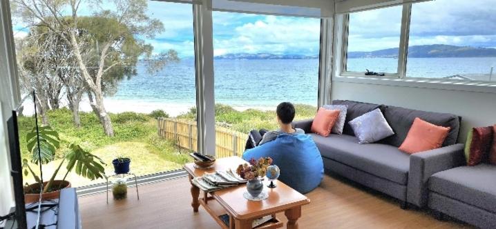 a person sitting on a couch looking out at the ocean at Beach Getaway - Blessington Villa in South Arm