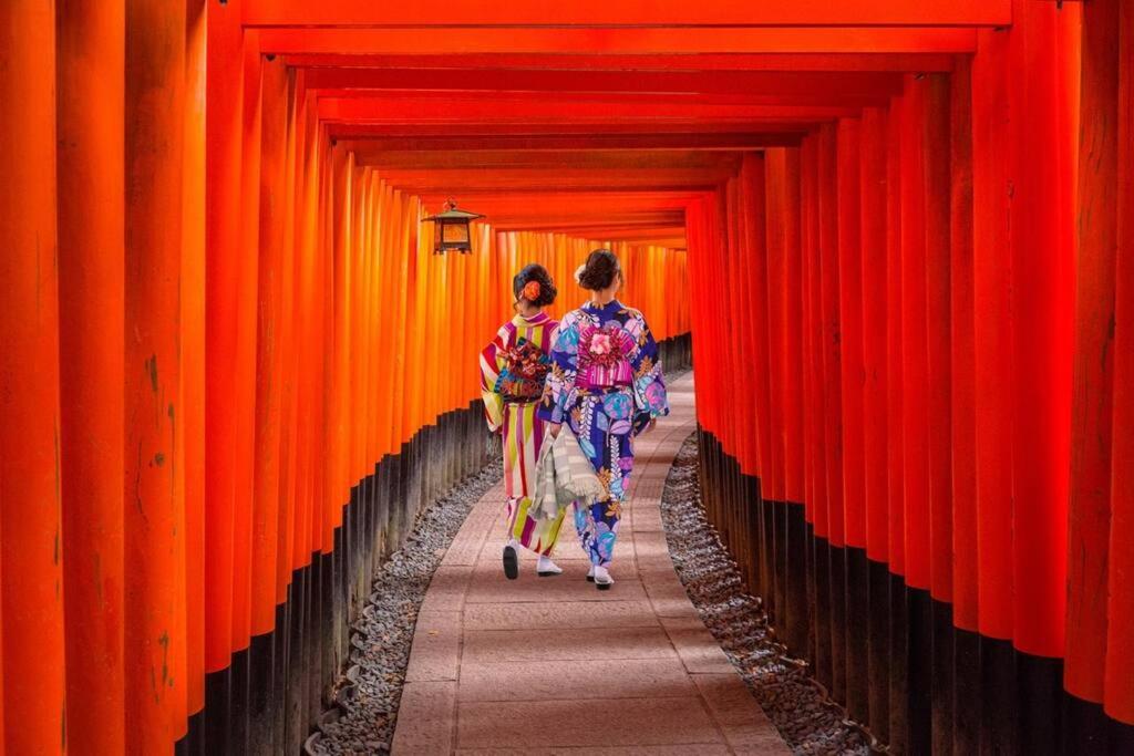 two women walking down a hallway of orange walls at 稲荷 かおり in Kyoto