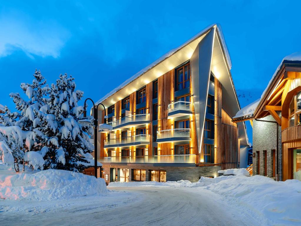 un grand bâtiment dans la neige avec un arbre dans l'établissement Hôtel Le Diamond Rock, à Tignes