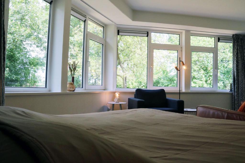 een slaapkamer met een bed, een stoel en ramen bij Eco Lodge Drenthe in Valthe