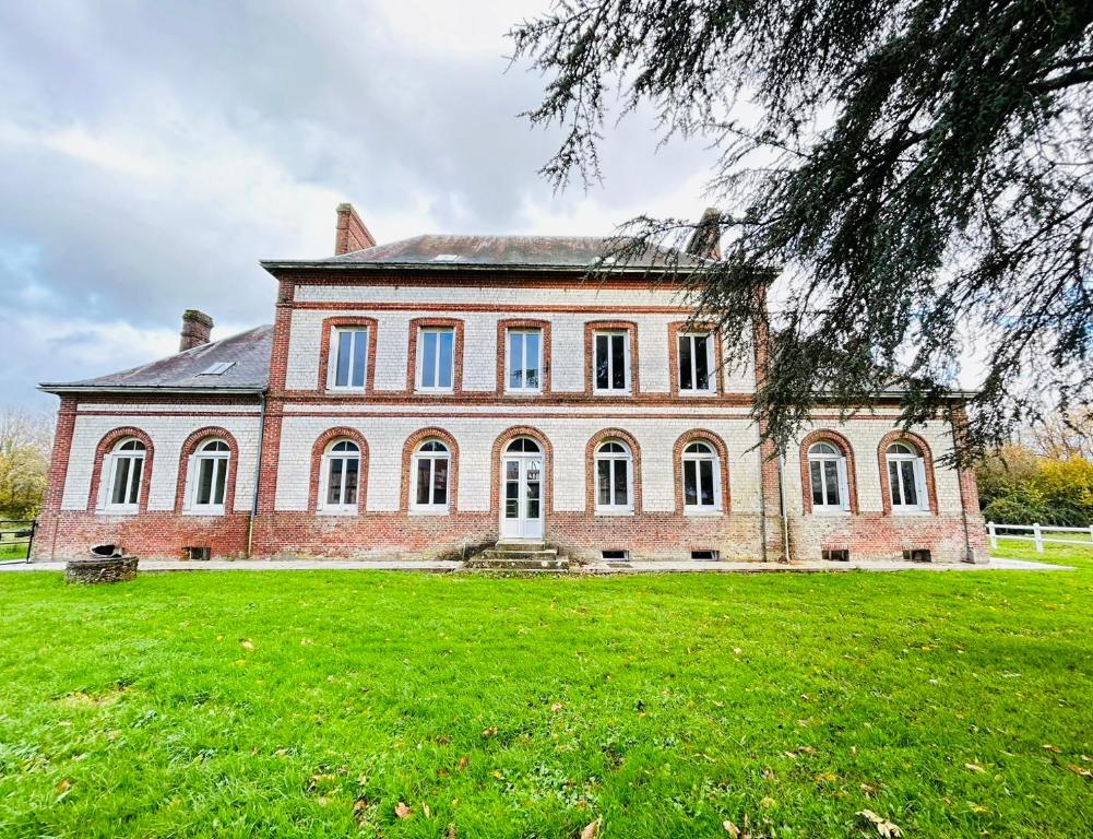 Un gran edificio de ladrillos en un campo de hierba. en Gîte de groupe à la Ferme de Verdun, 1H30 de Paris, en Le Héron
