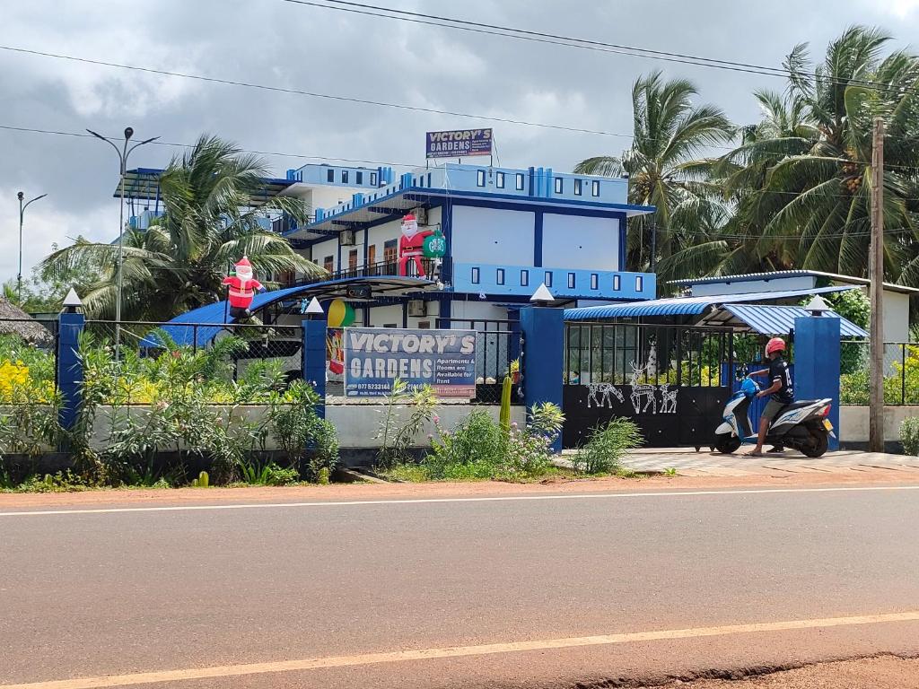 a man riding a scooter in front of a blue building at Victory's Gardens in Mannar