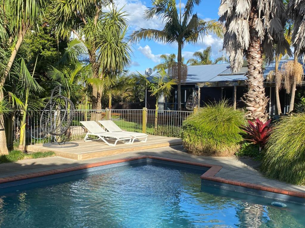 a swimming pool with a bench and palm trees at Garden Oasis in the heart of Pāpāmoa in Tauranga