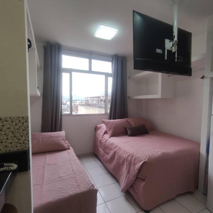 a room with two beds and a tv and a window at Kitnet no centro de Guarapari in Guarapari