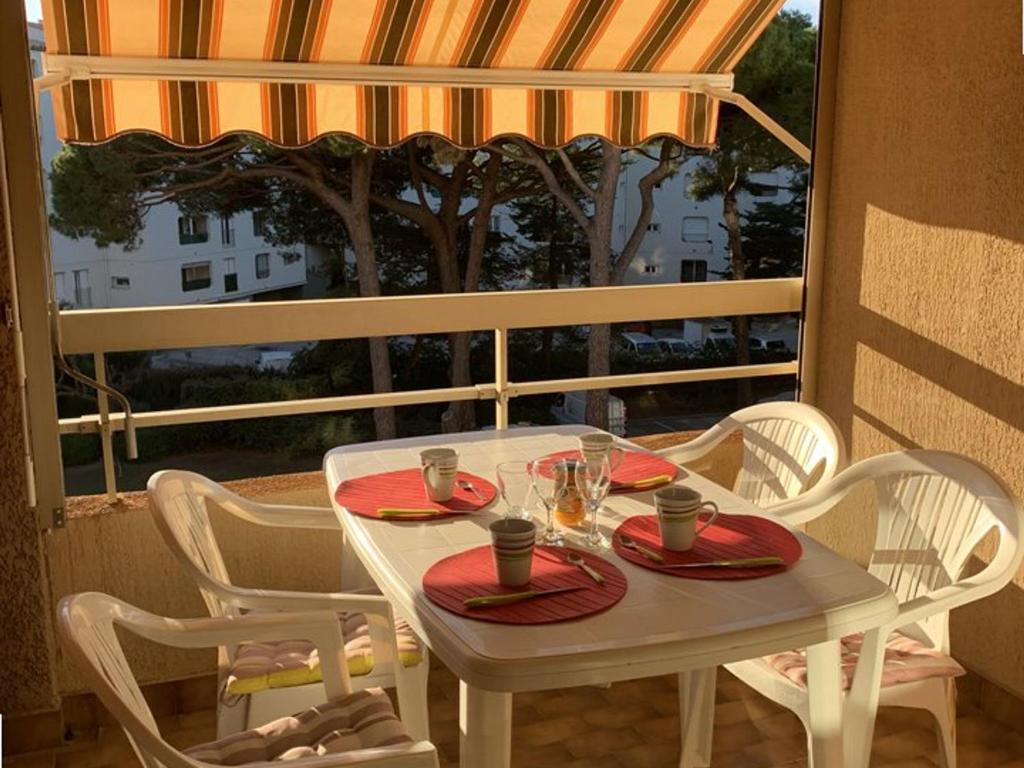 une table blanche avec des assiettes rouges et des verres sur un balcon dans l'établissement Hyères Port : T2 avec Loggia, WIFI, Parking, Climatisation, 4 Pers., Proche Plaisance - FR-1-335-164, à Hyères