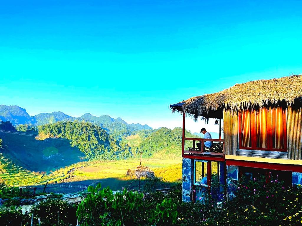 a man sitting on the balcony of a thatch hut at Mộc Châu Peachy Garden in An Pon