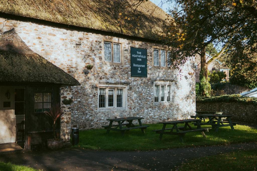 un edificio de piedra con mesas de picnic delante de él en The Heathfield Inn en Honiton