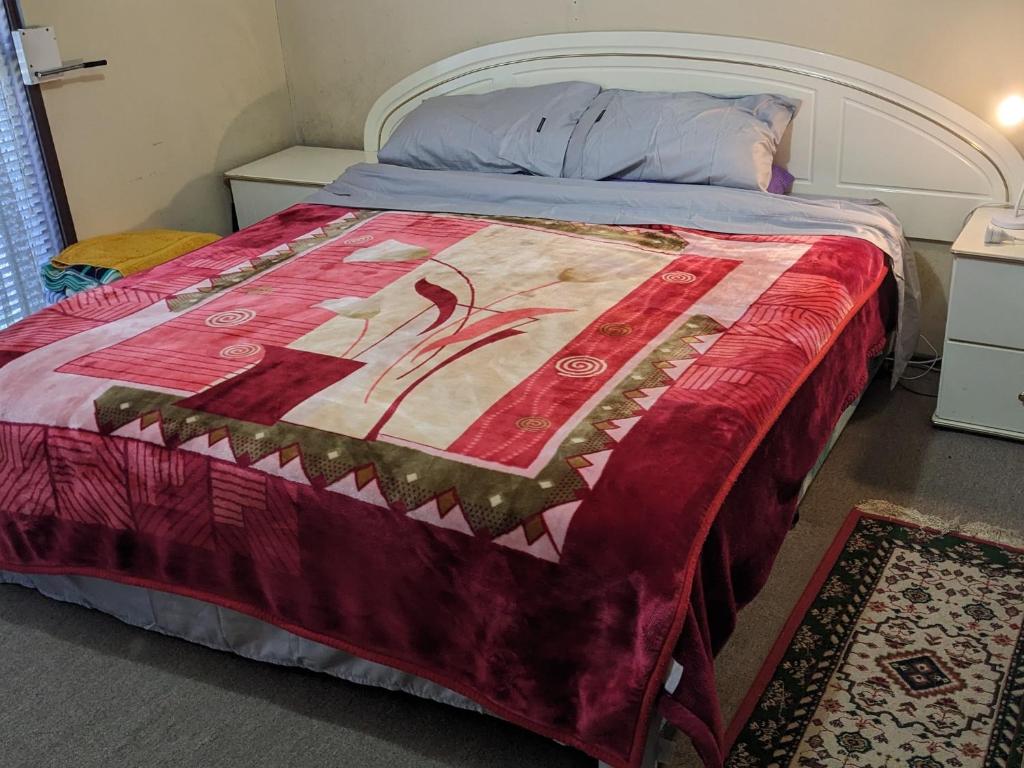 1 dormitorio con 1 cama con edredón rojo en Homestay - Large Private Room With A King Size Bed - SHARED Bathroom FREE Kitchen Essentials Milk, Bread, Tea, Coffee and Cereal WIFI HDTV FREE Laundry Service Meal and Transportation services available on request, en Bidwill
