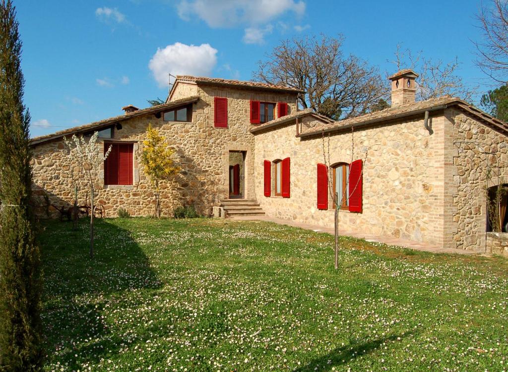 a stone house with red shutters on a field of grass at La Capanna di Panpepato in Rosia