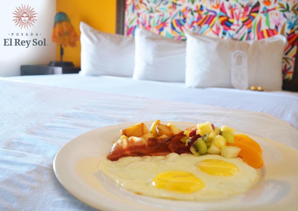 a plate of food with eggs and fruit on a bed at Hotel Posada El Rey Sol in Ensenada