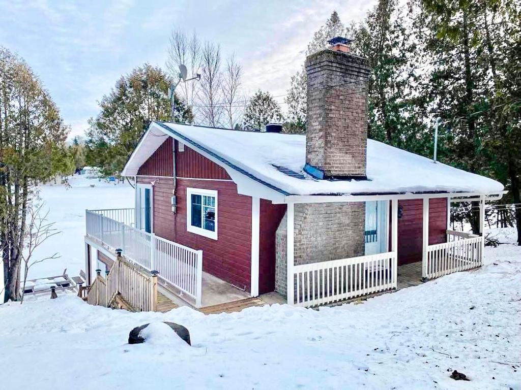 una casa roja con techo cubierto de nieve en la nieve en Chalet bord de l'eau et sentier, en Mont-Laurier