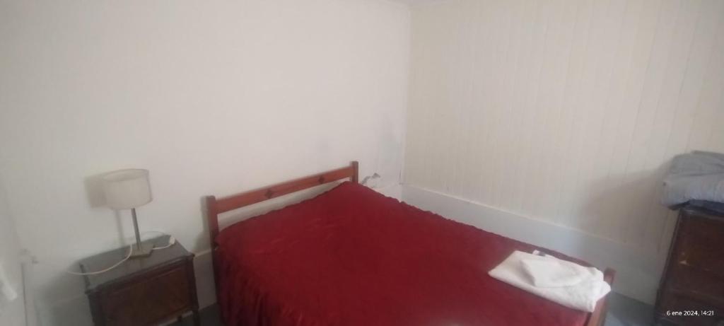 Cama roja en habitación blanca con lámpara en Departamento Esquel en Esquel