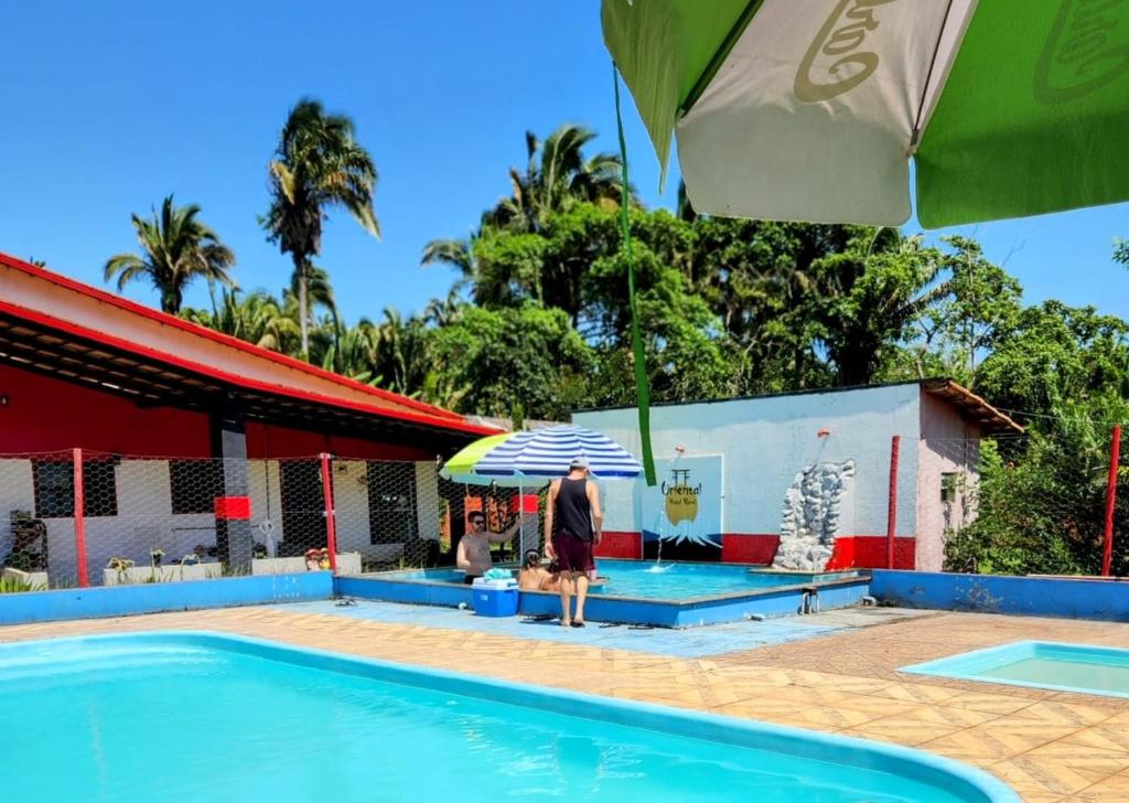 a man standing next to a swimming pool with an umbrella at Pousada Recanto Oriental in Palmas