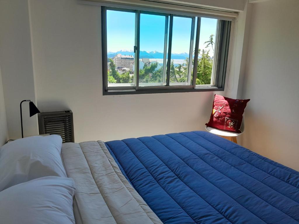 um quarto com uma grande cama azul e uma janela em MIRADOR DEL CENTRO BARILOCHE em San Carlos de Bariloche