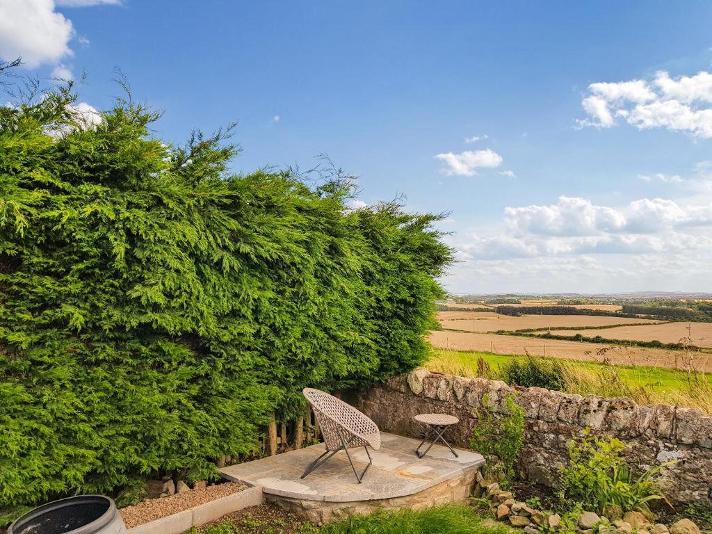 a chair and stool sitting on a stone bench next to a wall at Maines Farm Cottage in Chirnside