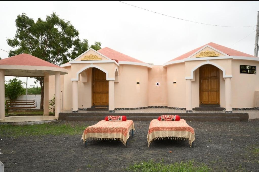 two beds in front of a building with two doors at Kutch kutir in Bhuj