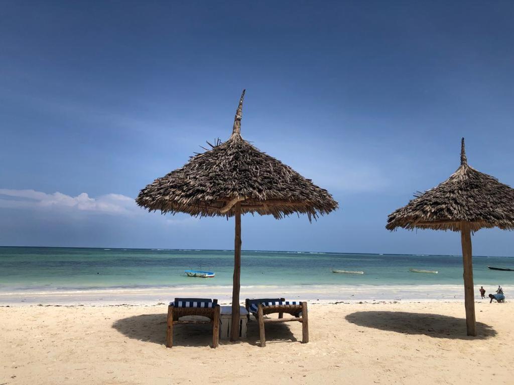 two straw umbrellas and chairs on a beach at Waka Waka in Pwani Mchangani