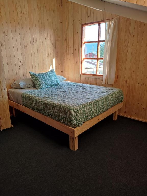 uma cama de madeira num quarto com uma janela em Verdeagua Hostal em Chaitén