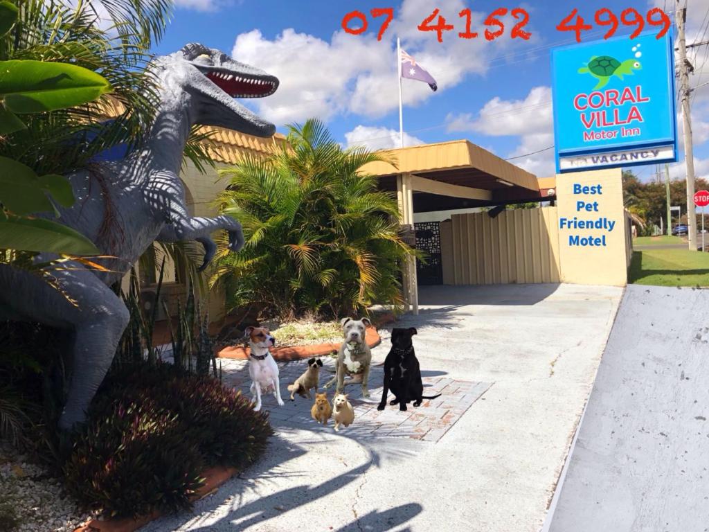un grupo de perros parados junto a una estatua de dinosaurio en Bundaberg Coral Villa Motor Inn, en Bundaberg