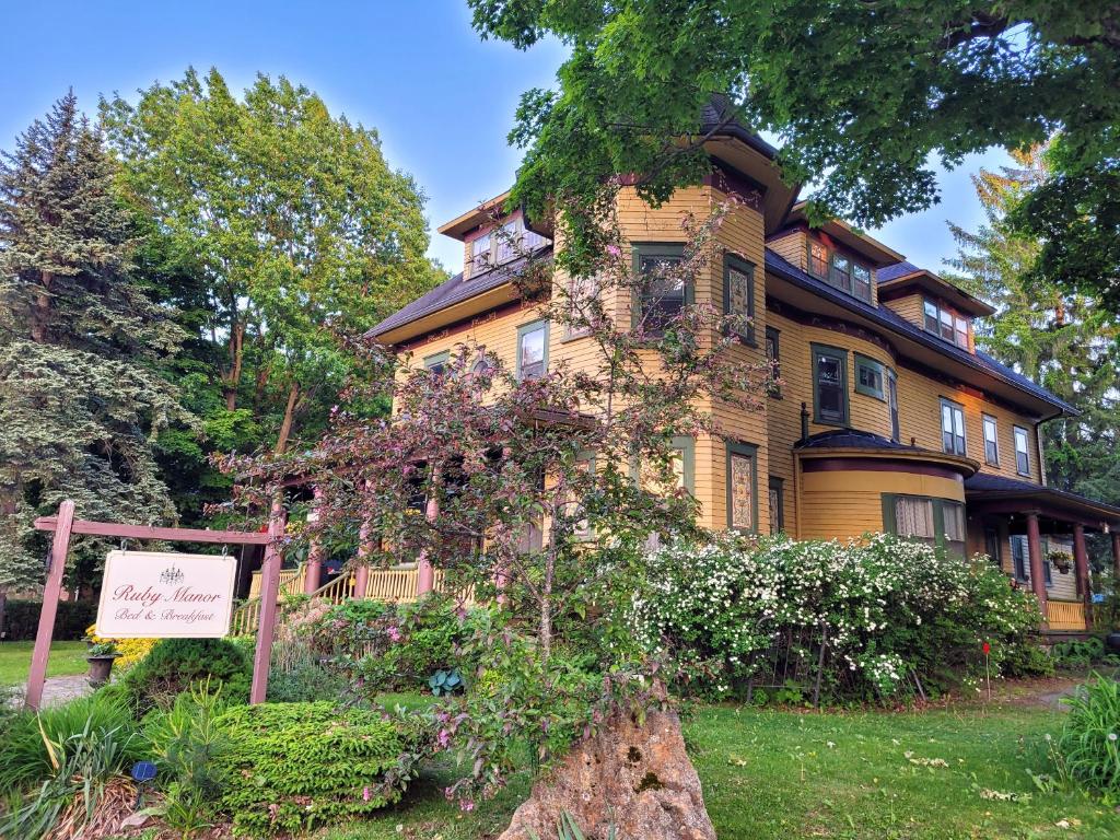 une grande maison jaune avec un panneau devant elle dans l'établissement Ruby Manor Bed & Breakfast, à Gananoque