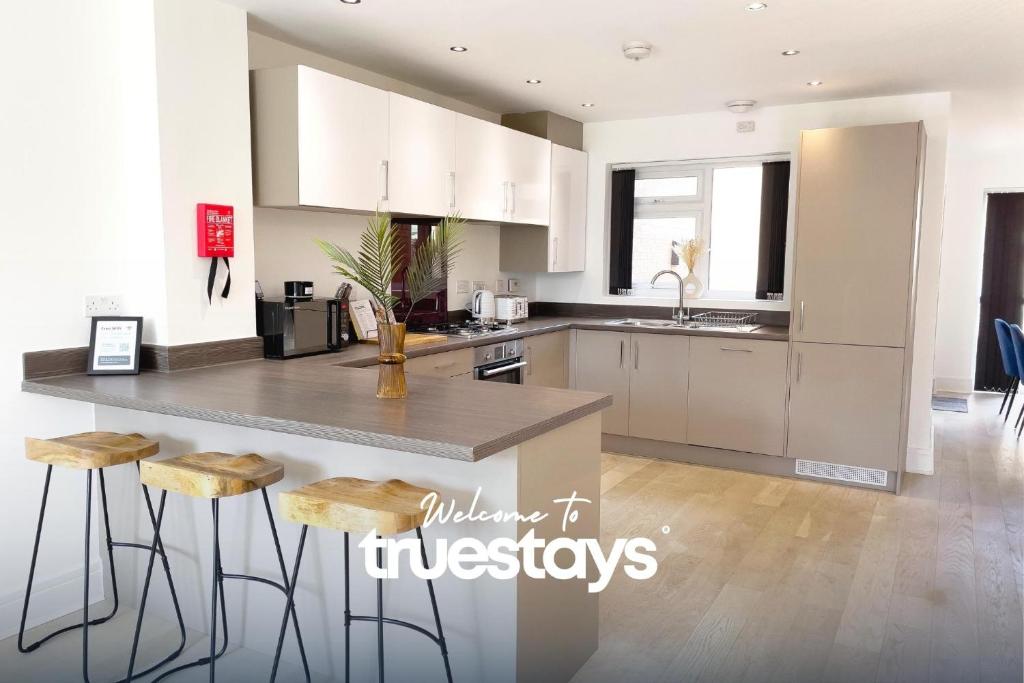 a kitchen with white cabinets and a island with stools at Bridgewater House by Truestays - NEW 3 Bedroom House in Stoke-on-Trent in Etruria