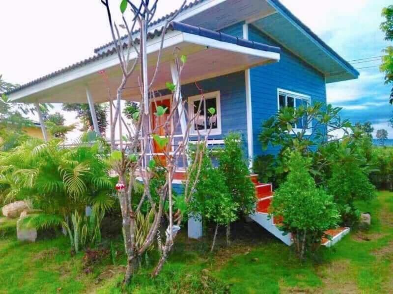 a blue house with a porch and some plants at อุดมทรัพย์วิลเลจฟาร์ม in Ban Huai Nam Khem
