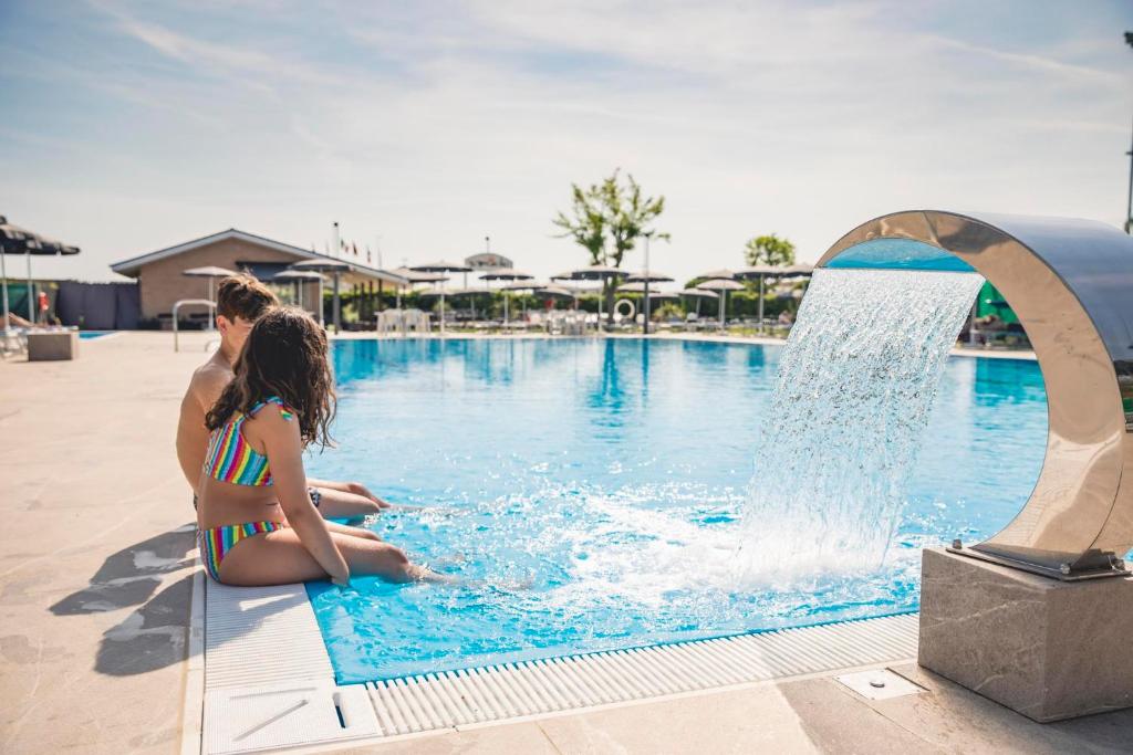 Eine Frau und ein Mädchen, die neben einem Pool sitzt. in der Unterkunft Hotel Baya - in centro, sul mare in Milano Marittima