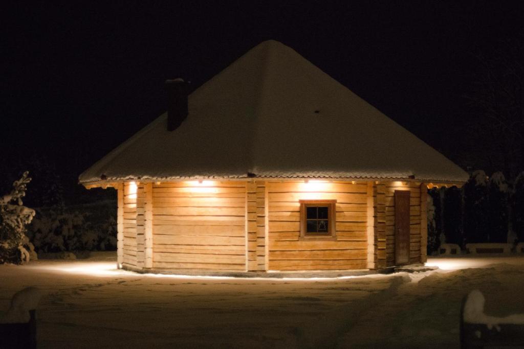 una pequeña casa de madera con luces encendidas por la noche en Ziedu pirts, en Auciems