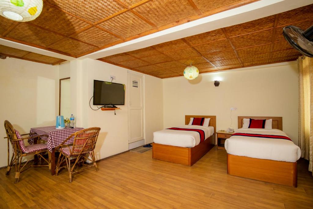 Una habitación con dos camas y una mesa y un televisor. en The Muglan Hotel and Restaurant, en Bhaktapur