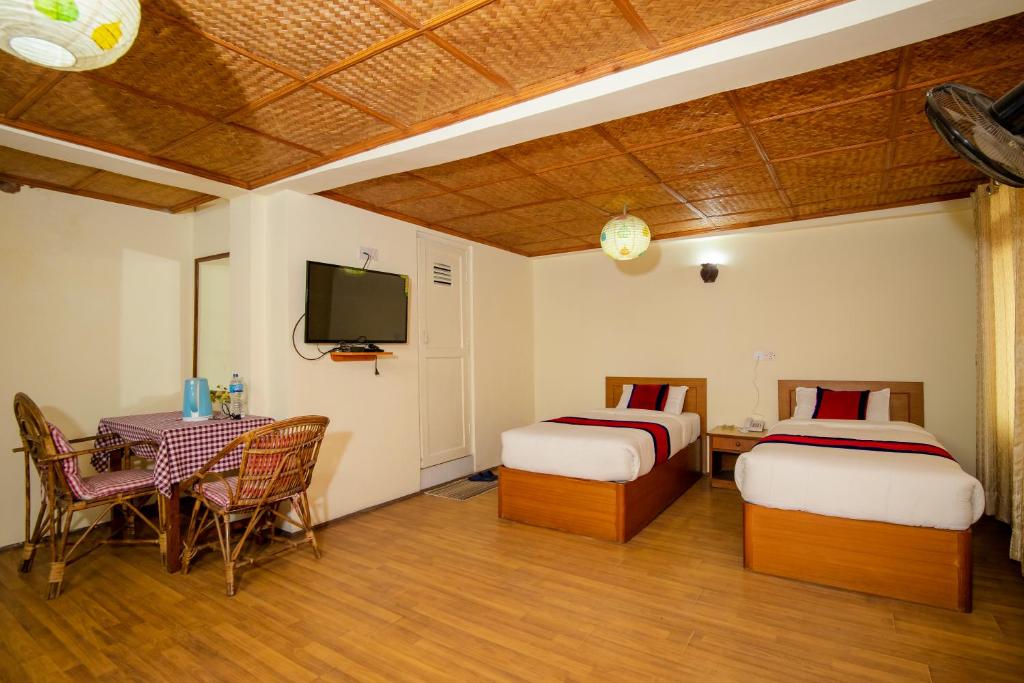 a room with two beds and a table and a tv at The Muglan Hotel and Restaurant in Bhaktapur