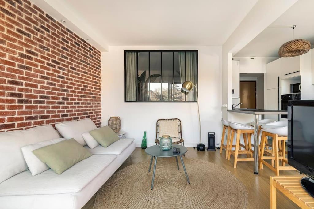 uma sala de estar com um sofá branco e uma parede de tijolos em Le Jules de Toulouse em Toulouse