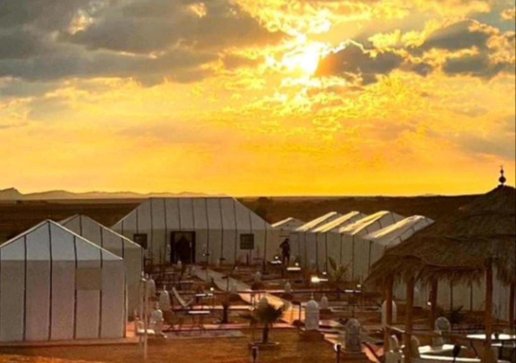 eine Gruppe weißer Gebäude mit Sonnenuntergang im Hintergrund in der Unterkunft Fantastic Desert Luxury Camp in Merzouga