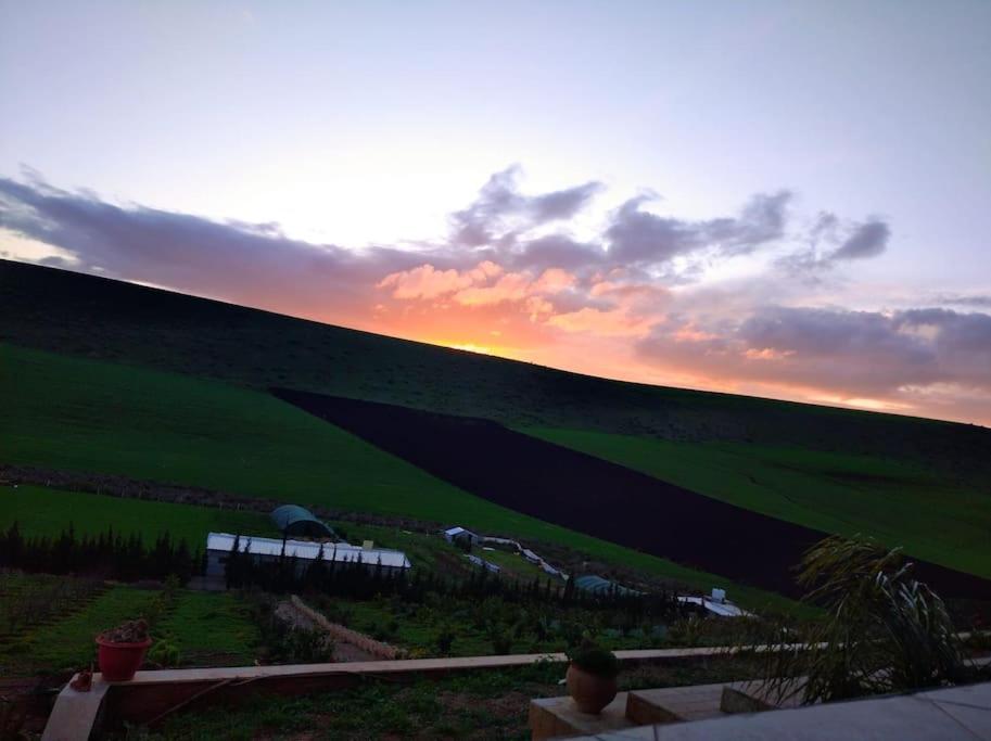 a sunset over a hill with a green field at Maison de campagne Benslimane 