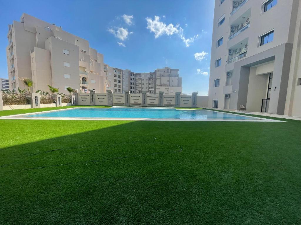 a large swimming pool with green grass in front of buildings at Un appartement S+1 agréable et spacieux ( terrasse) in Nabeul