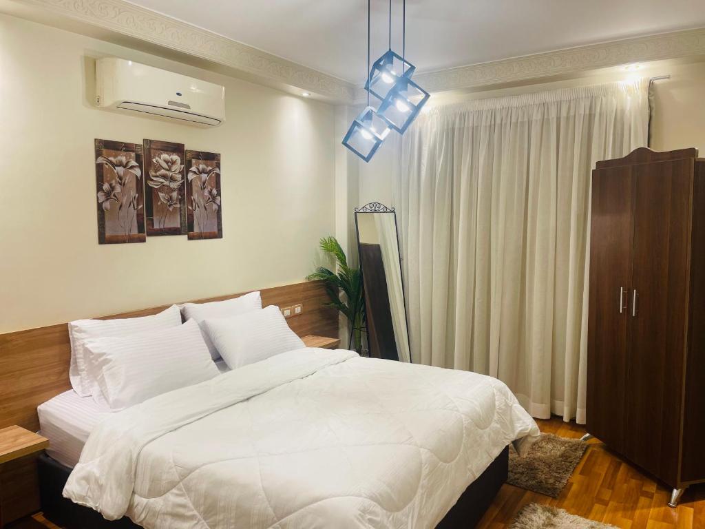 - une chambre avec un lit blanc et une lampe pendant dans l'établissement Mokattem private Condo, au Caire