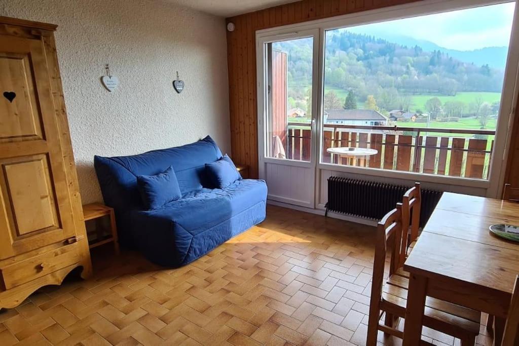 a living room with a blue couch and a large window at Studio cabine au cœur de la montagne Les Memises in Thollon