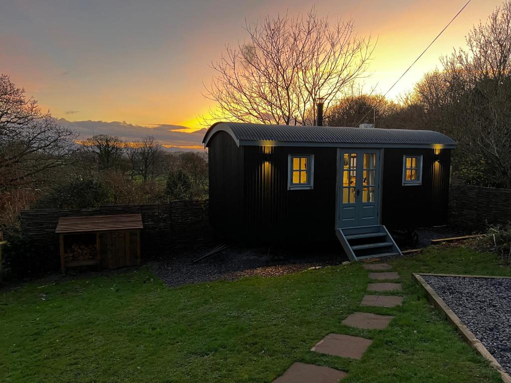 een zwart tiny house met een zonsondergang op de achtergrond bij Modern Shepherd's Hut Retreat for 2, Dog Friendly in Llangoed