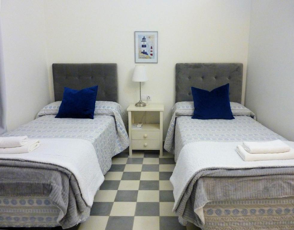 a bedroom with two beds with blue pillows and a checkered floor at APARTAMENTO APODACA in Cádiz