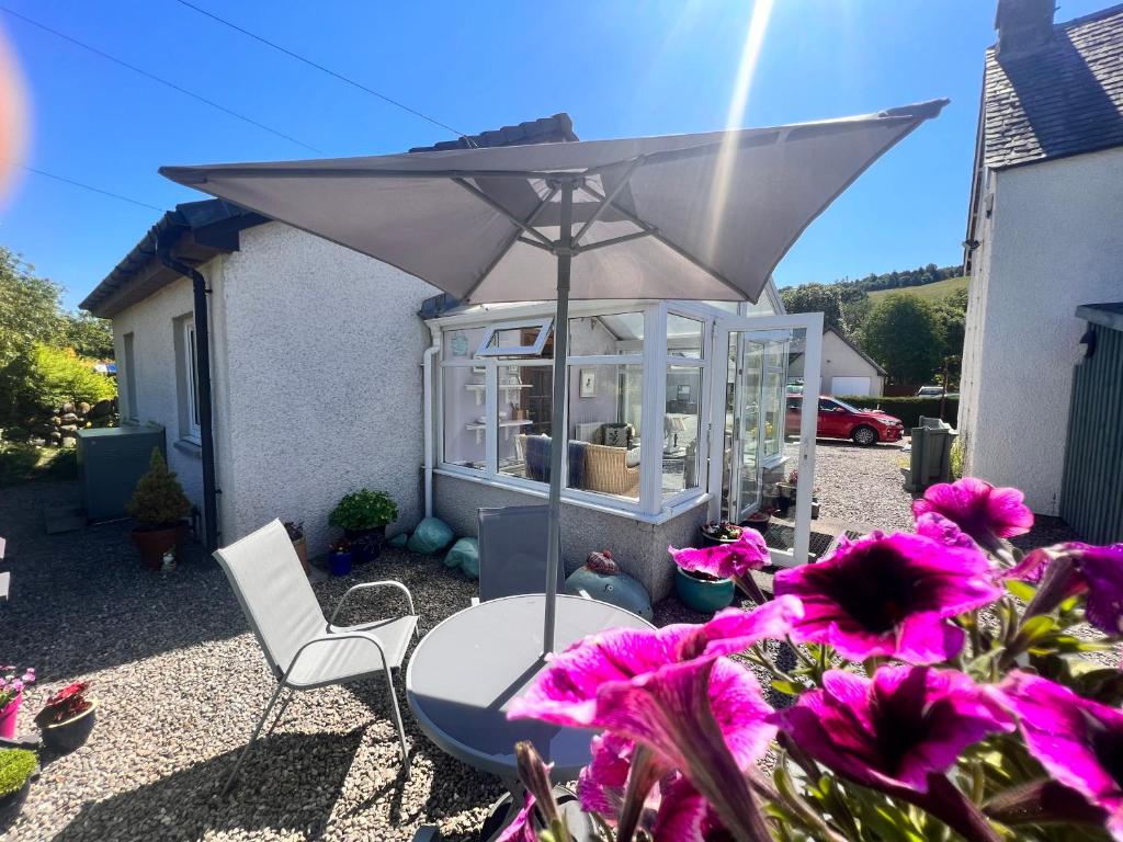 un patio con mesa, sombrilla y flores en Rooms at Elmbank near Loch Ness en Drumnadrochit