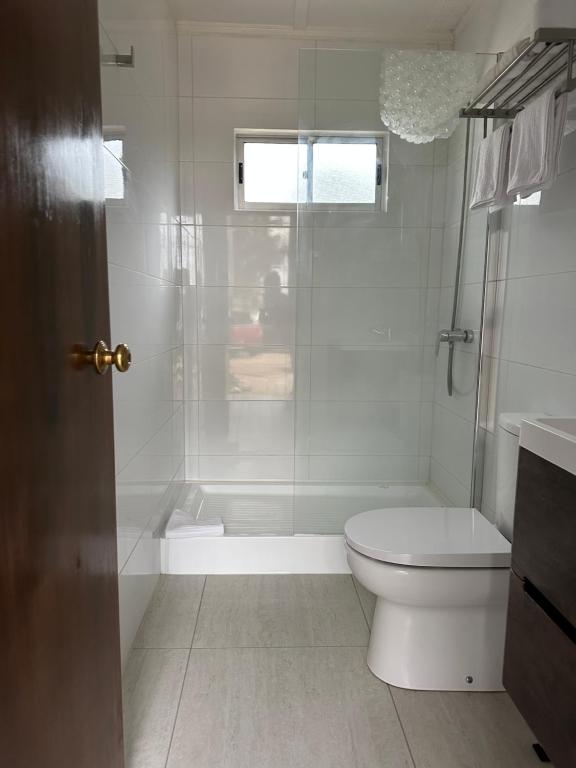La salle de bains blanche est pourvue d'une douche et de toilettes. dans l'établissement American Hotel, à Los Vilos