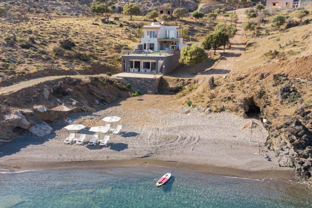 a house on a hill with a boat on the beach at Beachfront Studio Kyma East ~ Crete's Hidden Gem in Kali Limenes