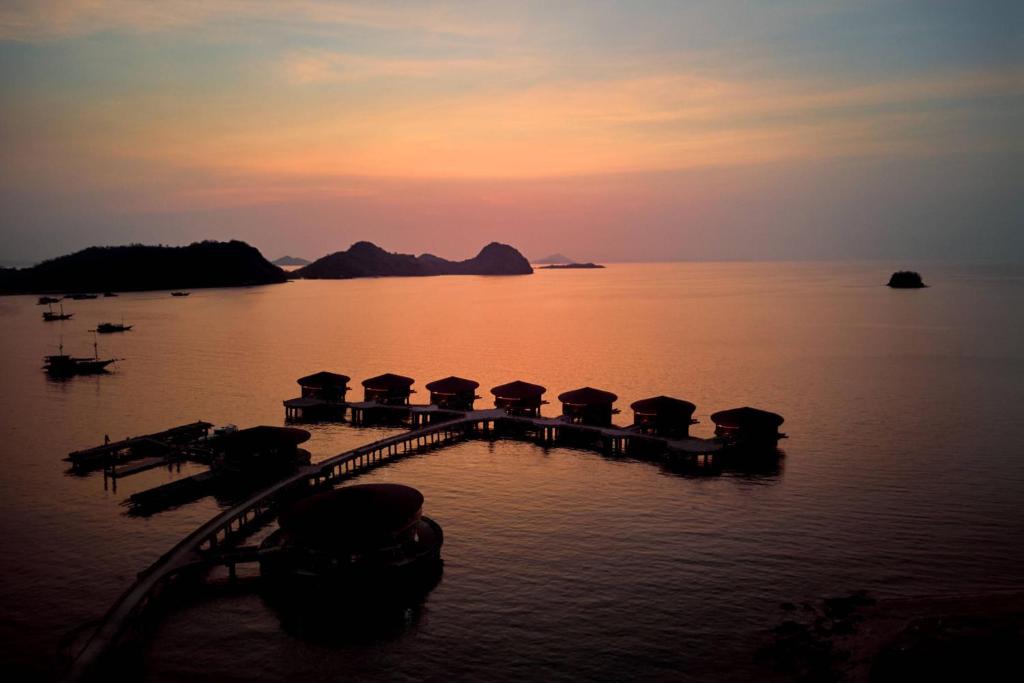 a pier with umbrellas in the water at sunset at TA’AKTANA, a Luxury Collection Resort & Spa, Labuan Bajo in Labuan Bajo