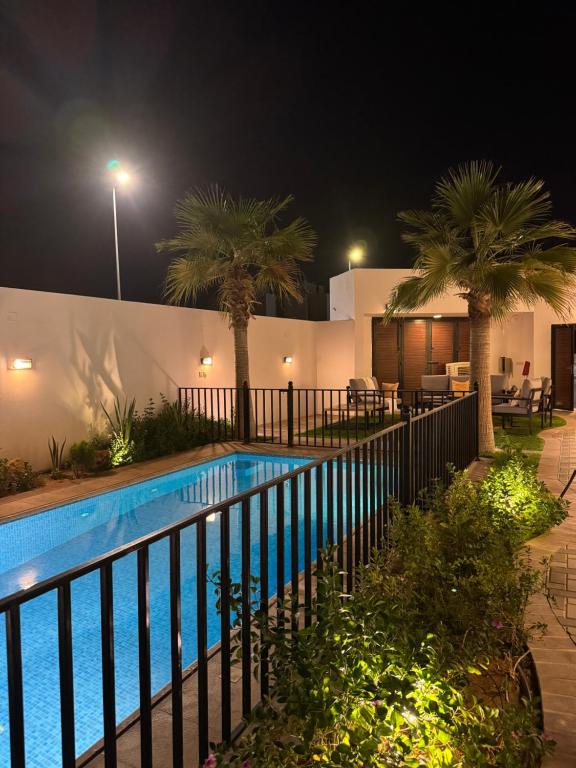 una piscina por la noche con una valla y palmeras en شاليه لونار, en Unaizah