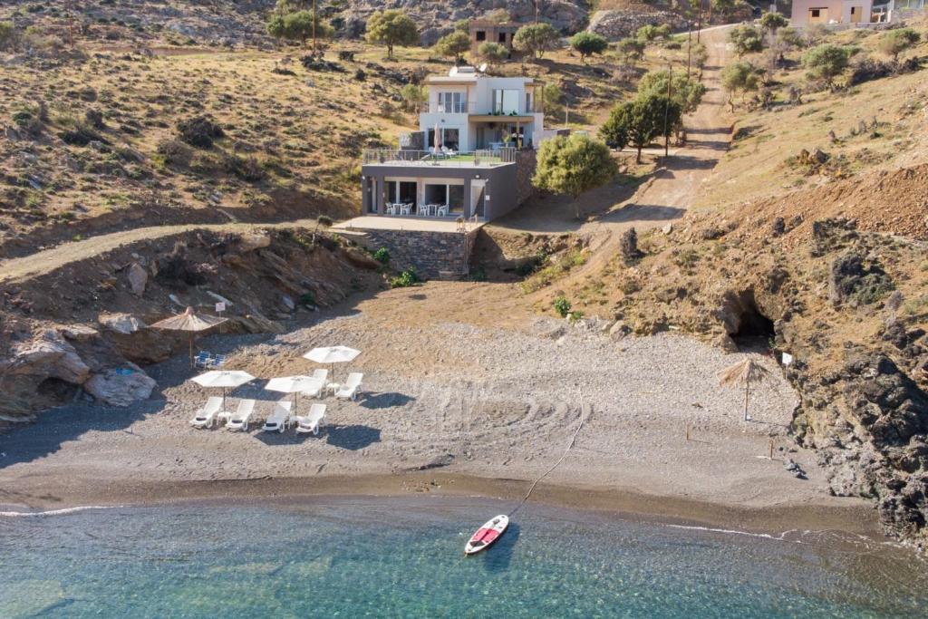 una casa en una colina con un barco en la playa en Beachfront Studio Kyma West ~ Crete's Hidden Gem, en Kalí Limenes